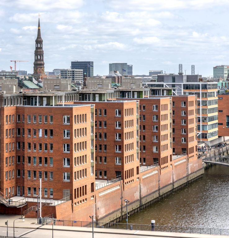 A rooftop view of a city with red brick buildings and historic church spires on the horizon. A blend of modern development and tradition. SSUCv3H4sIAAAAAAAAA41PQY6DMAz8i88gQSEV4SvVHkJiqFUgVWK2WqH8fR1KtdfNacYTz4x3IAc96FE1ldJV2TozlHU9VuVgL5eybXSjVKPRjA4KcIYR+rppdKtVpzp97a6VvAIGE8lCvwPN8xY5GCa/Qi9KwNVhOCA6Yh/IzMJSAZENbxGjrAmz4j2JevCP323Pcyko4XEbMkjFP2dfBZgJV/uT/VMuMqM54m4iPV6MYTmzPd9zxQyfgSyt09lJTvHLG6+e8+6RwN4+yJ3L7zPuJNOQs2B7zt44dKe8DQsxf2jAb8LX3++U0i8MgnvOhAEAAA==